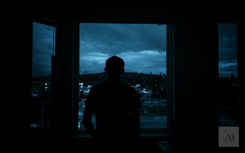 Figura solitaria ante una ventana nocturna lluviosa, representación adulta de la tristeza